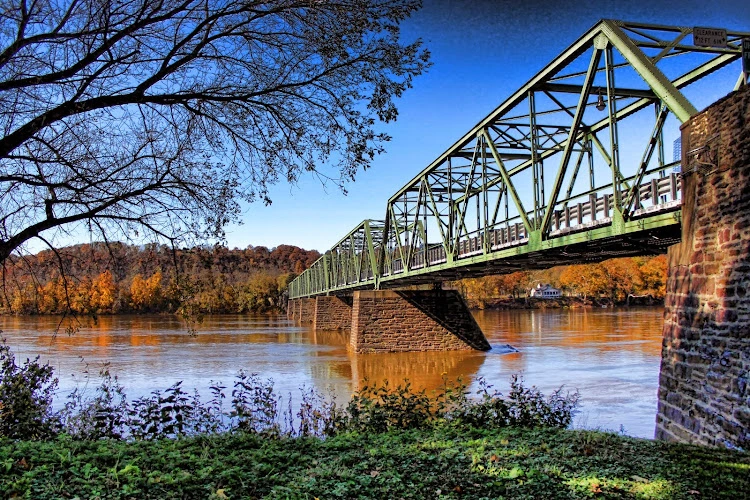 Steel truss bridge spanning river with bare trees and autumn foliage along banks