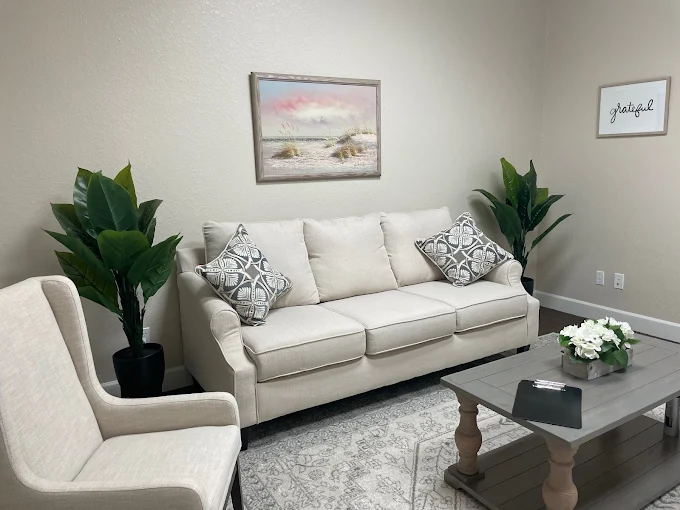 Welcoming waiting room with cream sofa, patterned pillows, potted plants, and beach landscape artwork