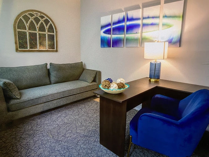 Modern therapy waiting room with gray sofa, blue armchair, decorative mirror, and abstract wall art