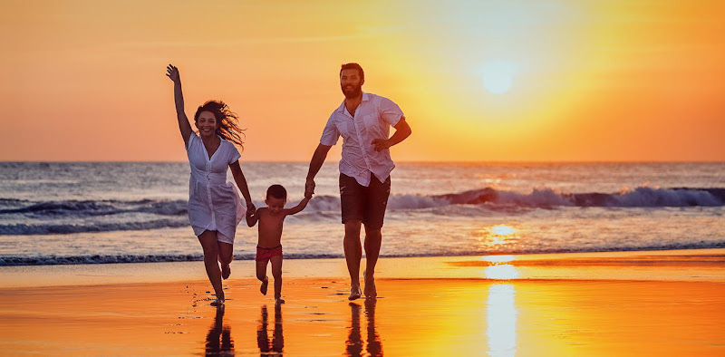 Family of three running together on beach at sunset with waves in background