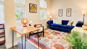 Bright therapy lounge with blue sofa, wooden table, colorful rug, and large windows