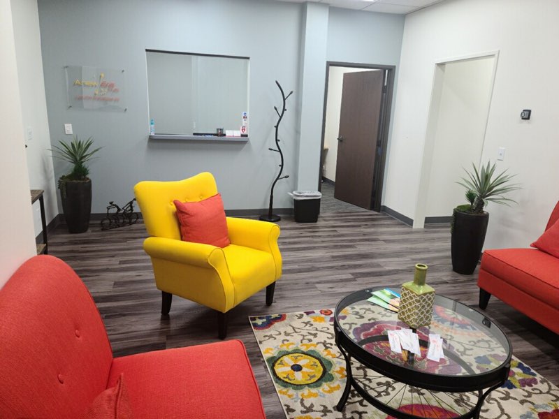 TMS therapy waiting room with red and yellow armchairs, colorful rug, and potted plants