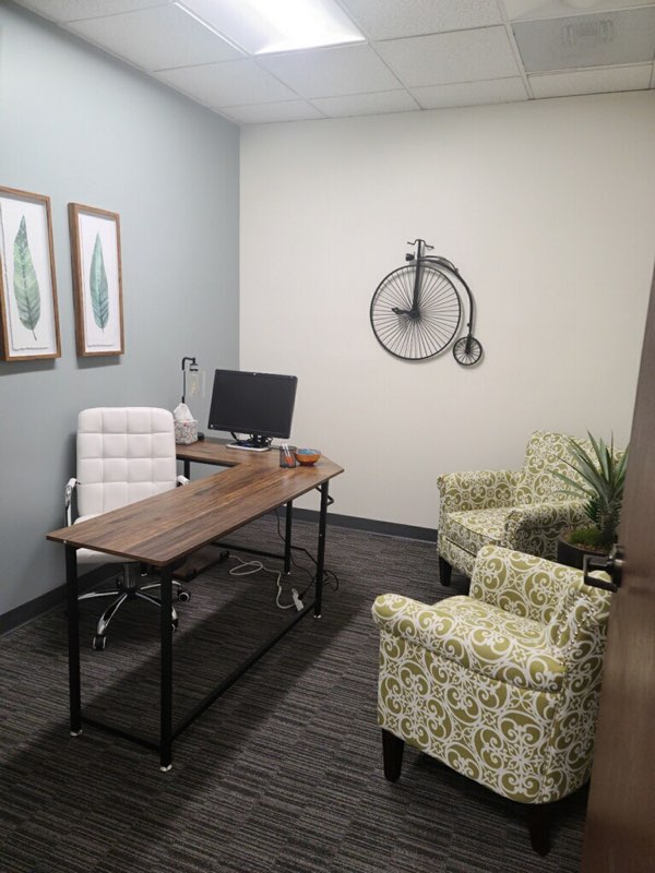 Private office space with desk, white chair, computer monitor, and seating area with plants
