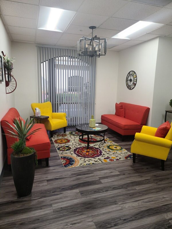 TMS therapy waiting area with red and yellow seating, patterned rug, and vertical blinds