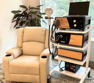 Beige recliner chair next to TMS equipment with orange and black devices stacked on mobile cart