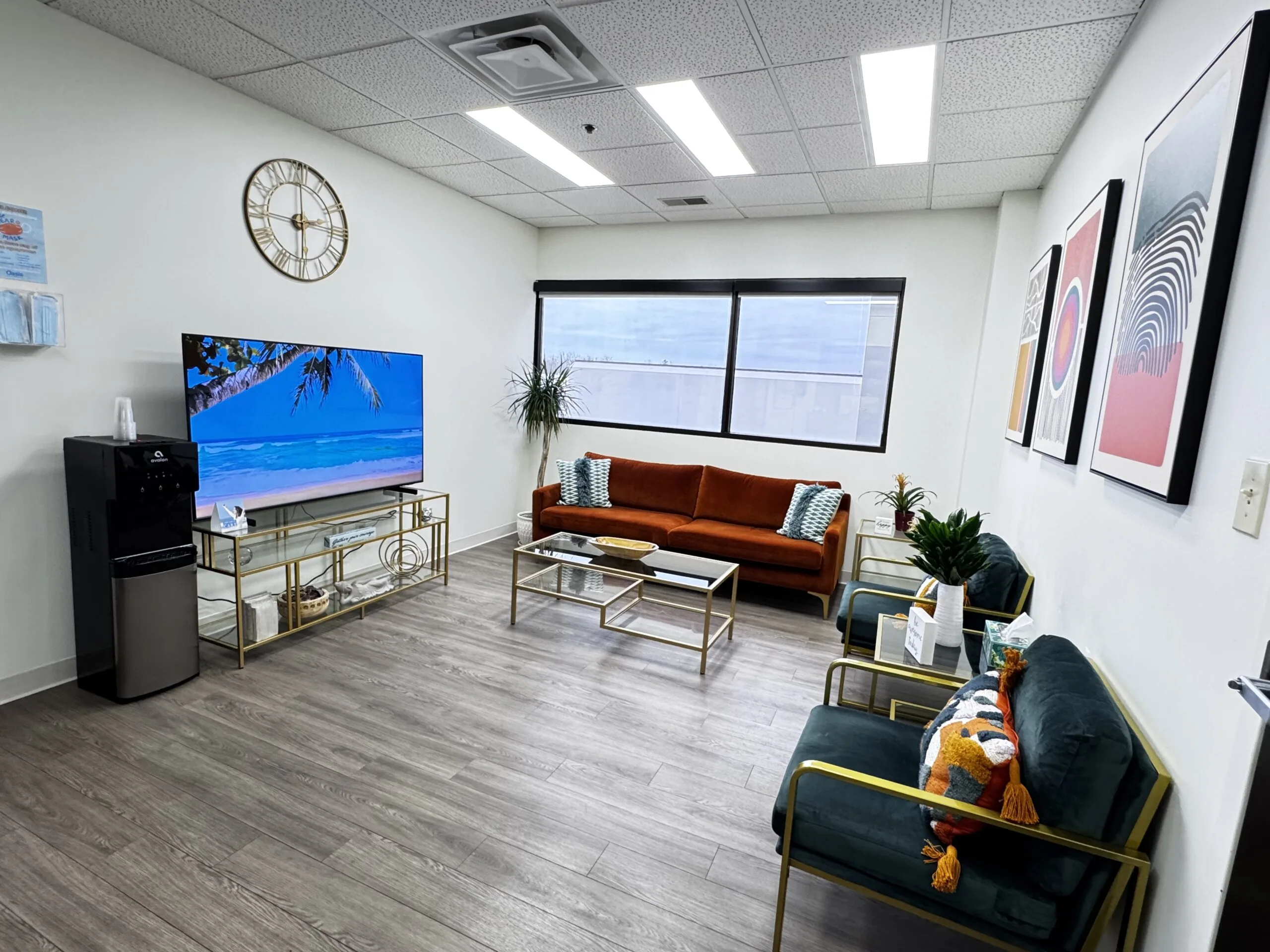 Waiting room with orange sofa, TV on stand, wall art, clock, and seating area