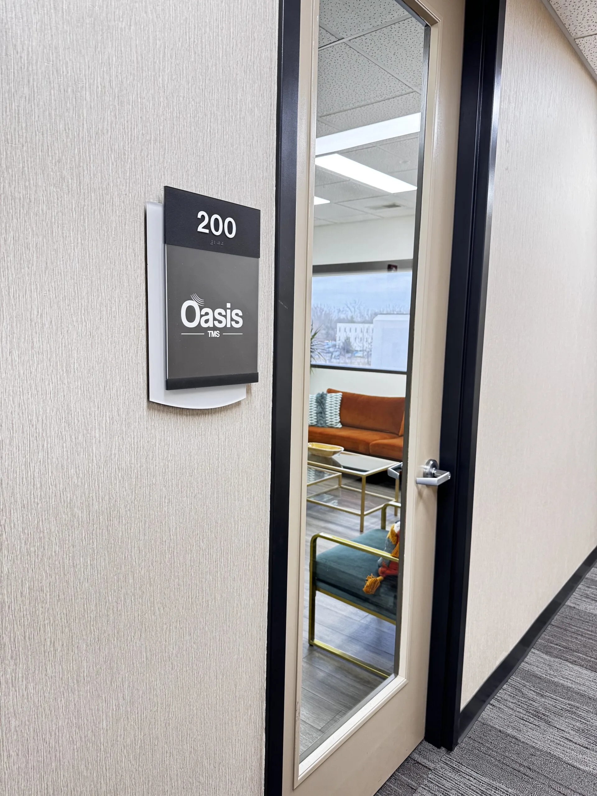 Oasis TMS suite 200 door sign with glass window showing treatment room interior