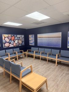 Waiting area with blue-cushioned seating arranged in U-shape, nature photography on dark walls, and wooden side table
