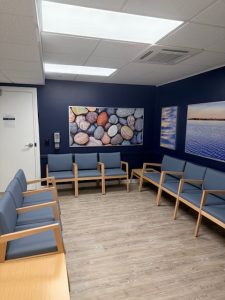 Waiting room with dark blue walls, multiple blue-cushioned chairs, and landscape artwork displays