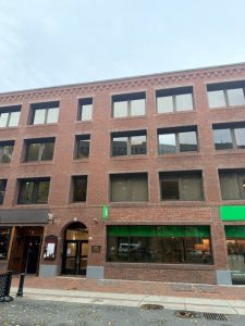 Brick storefront building exterior with large windows and green-lit ground-floor entrance