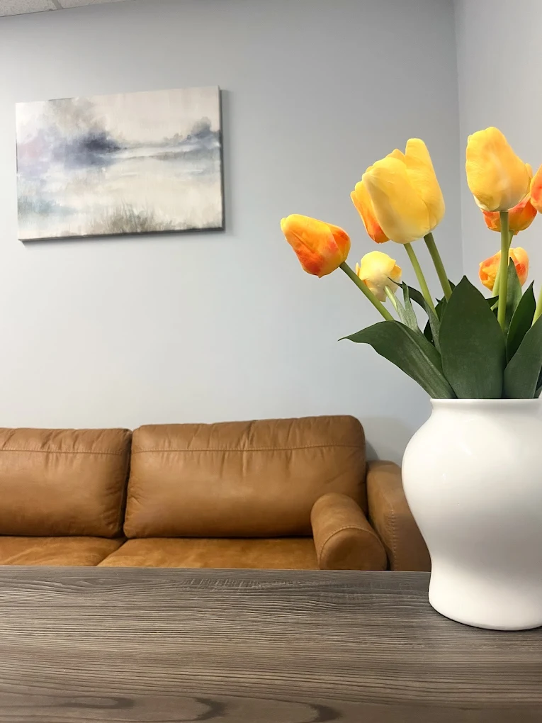 Waiting room with tan leather sofa, white vase of yellow and orange tulips, abstract landscape painting on wall