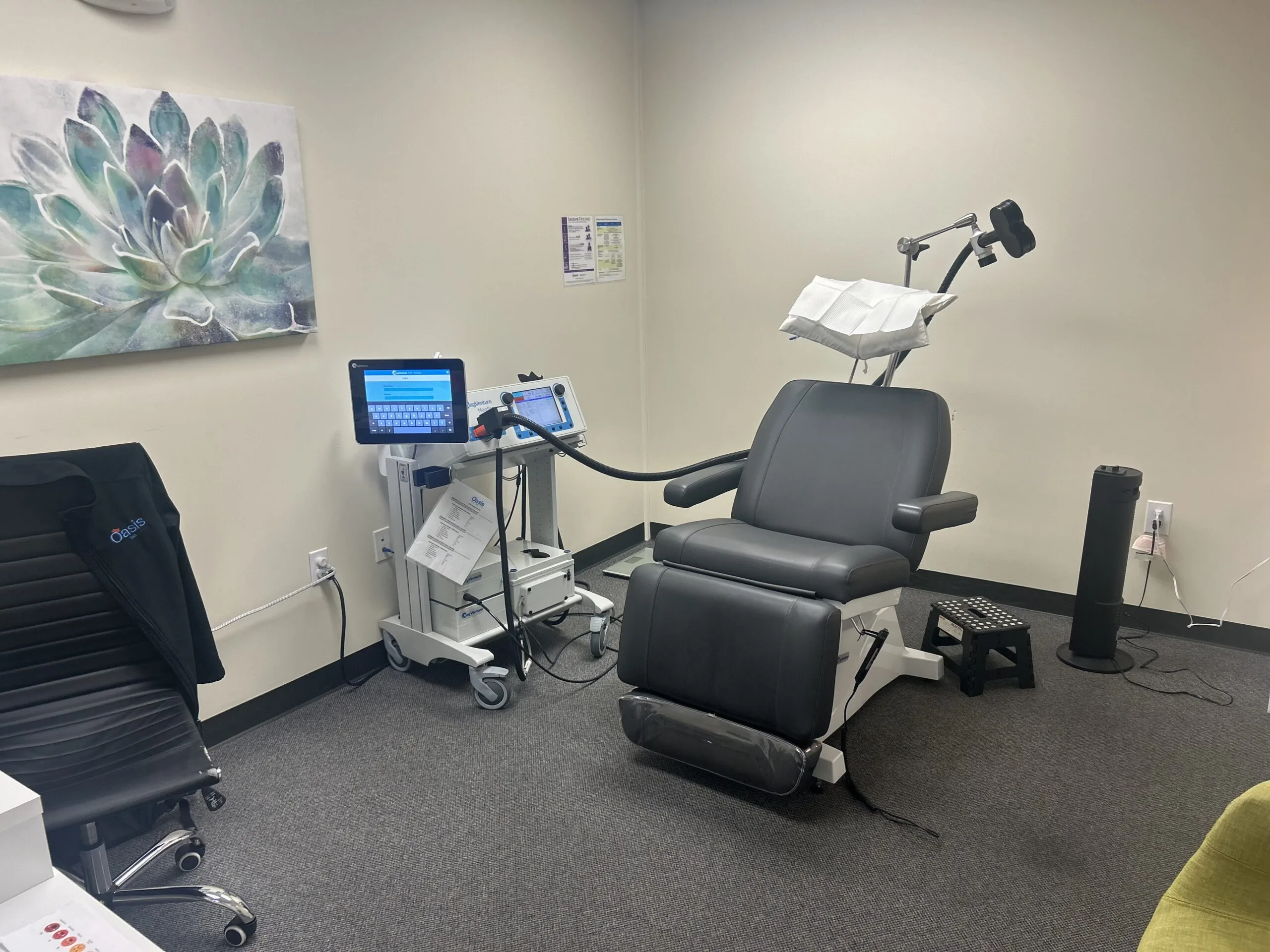 TMS treatment room with patient chair, desktop computer monitor, control system, and artwork