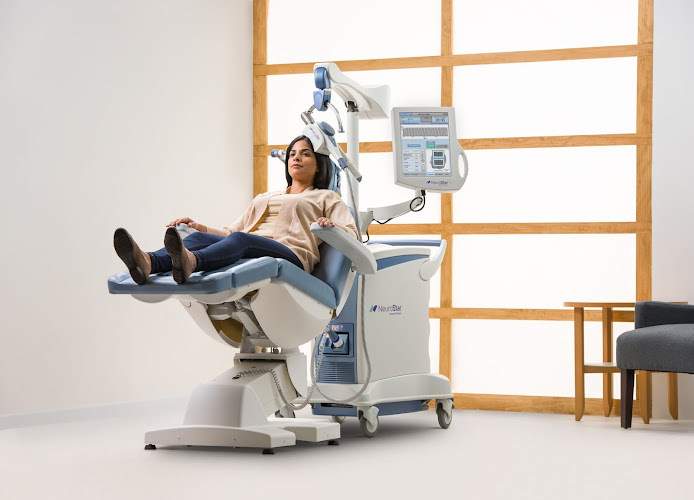 Patient seated in TMS treatment chair with transcranial magnetic stimulation device positioned above head