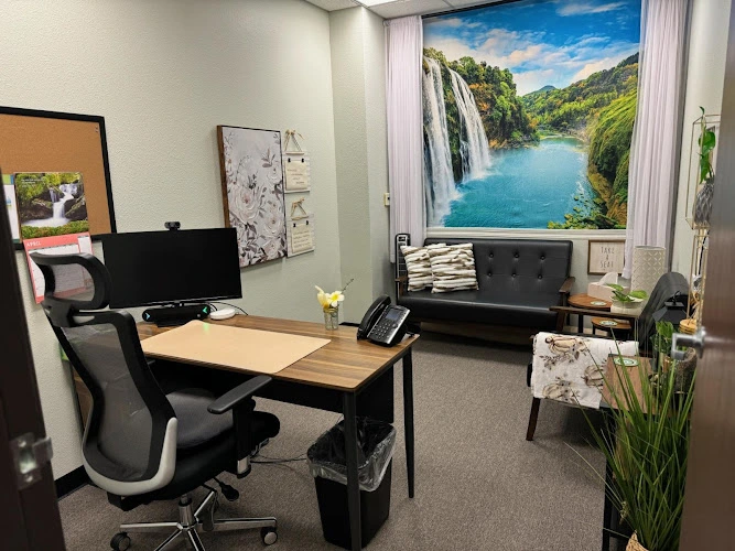 Mental health office with desk, computer monitor, black sofa, and waterfall landscape artwork
