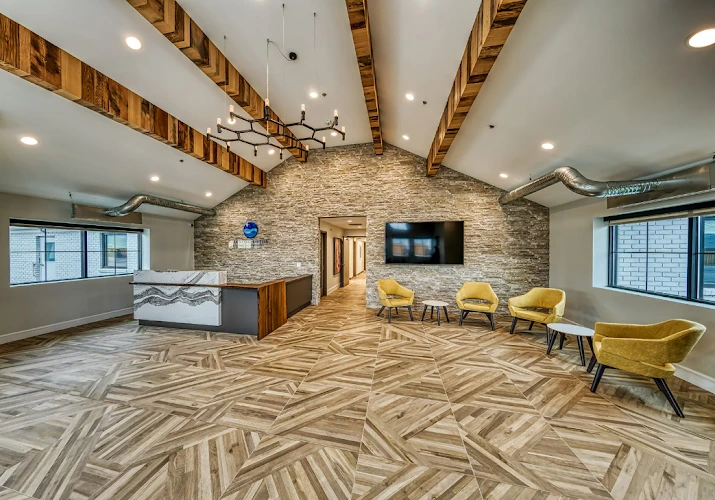 Modern rehab facility reception area with stone accent wall, wooden beams, yellow chairs, and TV display