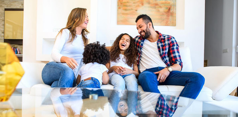 Family of four laughing together on a white couch in a bright living room
