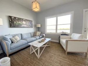 Modern therapy room with gray sofa, cream armchair, coffee table, and large windows overlooking water
