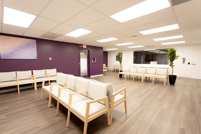 Spacious waiting room with wooden-framed cream seating, purple accent wall, potted plants, and modern lighting