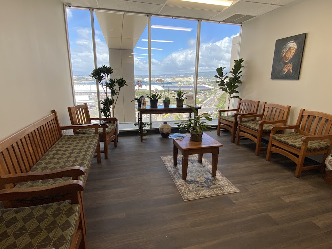 Waiting room with wooden chairs, plants, and floor-to-ceiling windows overlooking Hawaiian landscape