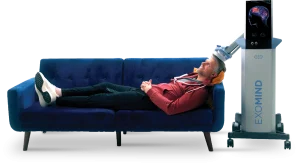 Man reclined on blue couch receiving TMS therapy with ExoMind device placed on his head showing brain visualization screen