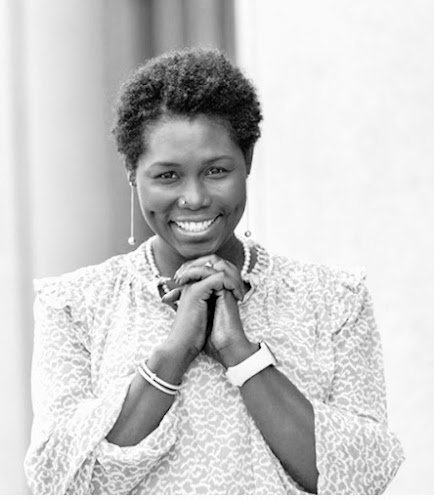 Professional headshot of smiling woman in light-colored textured shirt with hands clasped