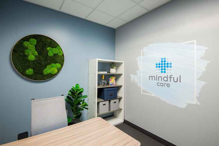Mindful Care office interior with blue accent wall, circular moss art, wooden desk, shelving unit, and illuminated company logo on wall