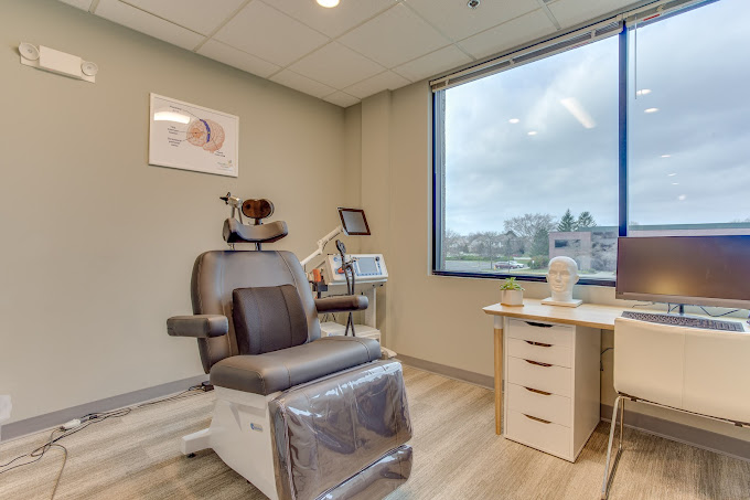 TMS treatment room with reclining chair, tablet devices, monitor, and large windows overlooking landscape