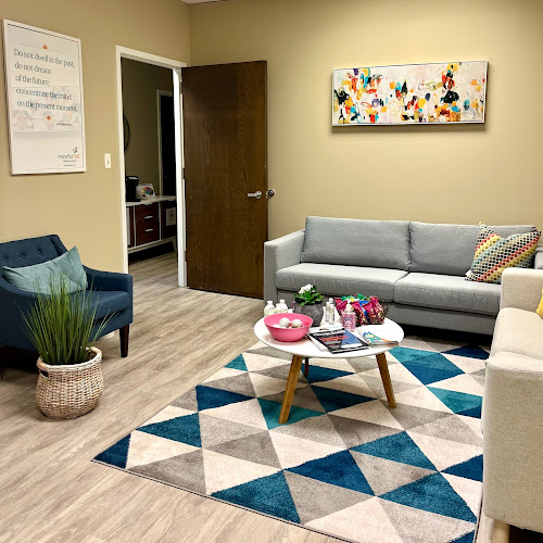 Mindful TMS waiting room with gray sofa, blue armchair, geometric patterned rug, and artwork on walls