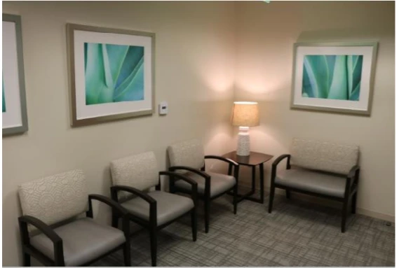 Psychiatry office reception area with gray upholstered chairs, side table, lamp, and framed artwork