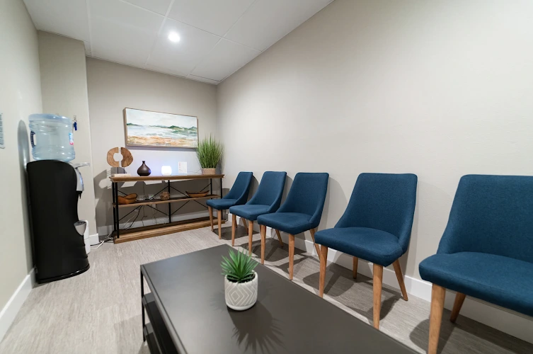 Modern waiting room with blue chairs, wooden console table, plants, and water cooler