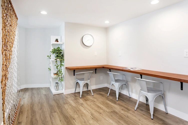 Minimalist consultation room with white chairs, wooden countertop, woven wall panel, and potted plant