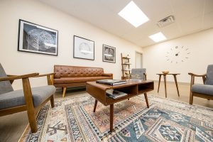 TMS therapy waiting room with mid-century furniture, leather sofa, patterned rug, and framed artwork on walls