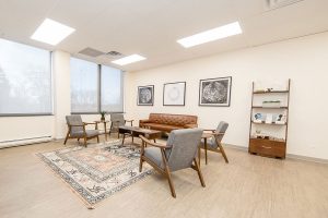 Modern clinic waiting room with mid-century furniture, grey chairs, tan sofa, and framed wall art