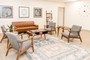 Spacious clinic lounge with tan leather sofa, grey chairs, wooden furniture, and large wall clock