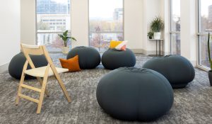 Contemporary office space with floor-to-ceiling windows overlooking city skyline, black seating poufs, and indoor plants