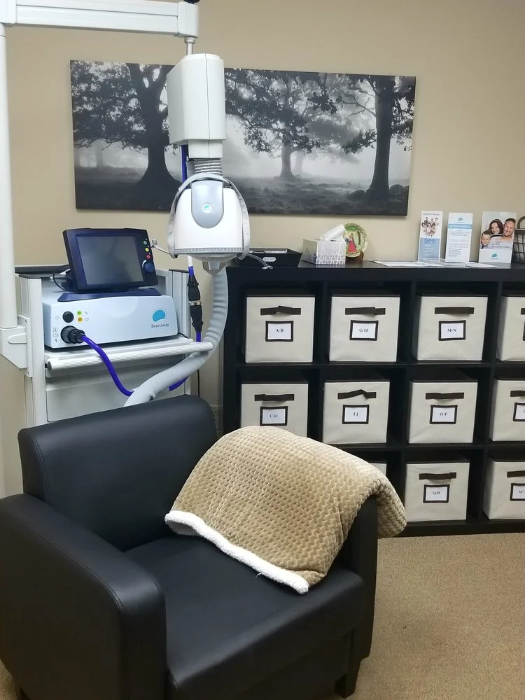 TMS treatment room with white device mounted above black patient chair and storage cabinet