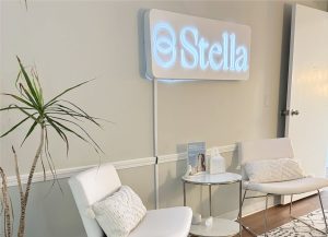 Stella neon sign illuminated above white chairs and a small table in a clinical waiting area