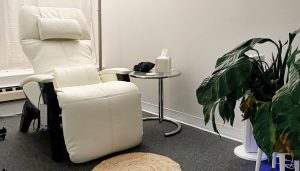 Cream-colored reclining chair next to side table with amenities in a treatment room with plants