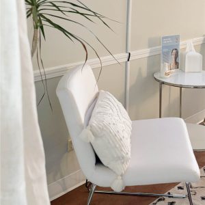 White modern chair with pillow near mirror and product display in a clinical waiting area