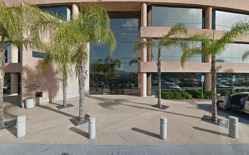 Modern medical building exterior with glass doors, palm trees, and parking lot