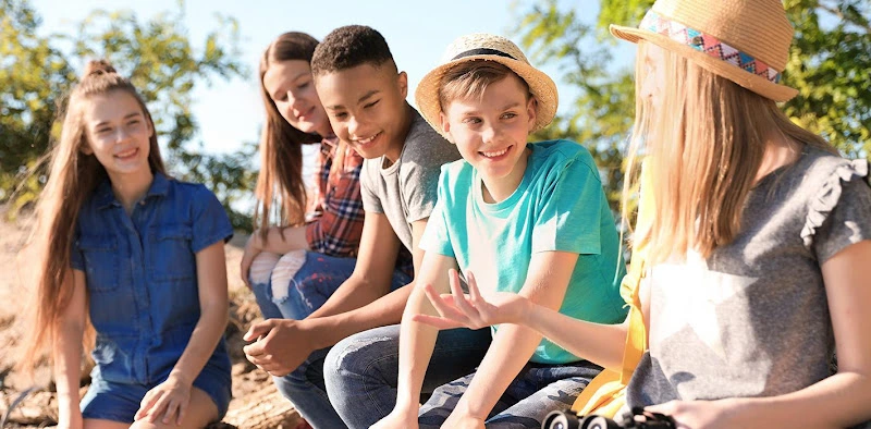 Group of five children sitting outdoors in a circle, smiling at the camera