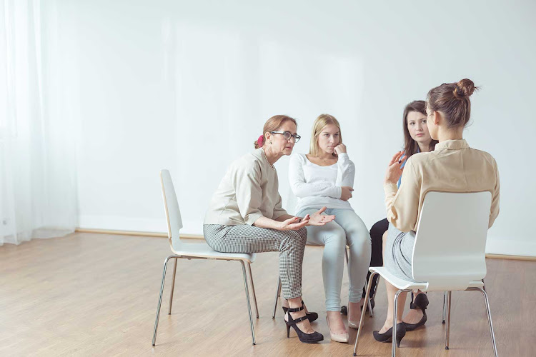 Group of five people sitting in a circle during a therapy session in a bright, minimalist room