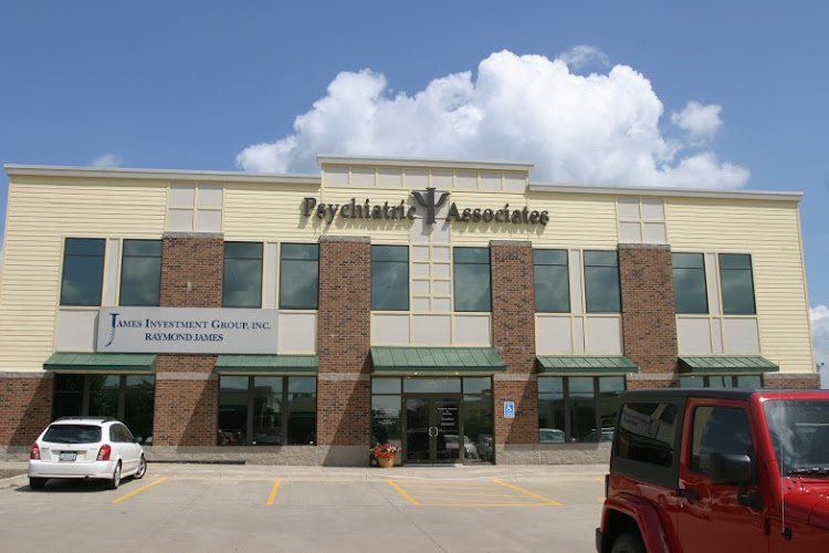 Psychiatric Associates medical office building with cream and brick facade, parked vehicles, and blue sky with clouds