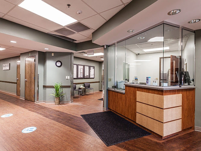 Medical office reception area with wood desk, glass partition, and waiting area with potted plant