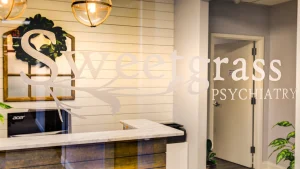 Sweetgrass Psychiatry reception desk with logo on wall and doorway to treatment area