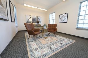 TMS therapy waiting room with two brown leather chairs, small table, and framed artwork on walls