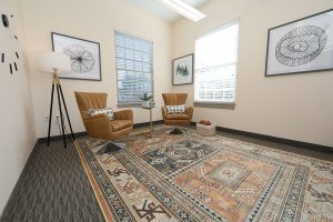 TMS therapy consultation room with two tan leather chairs, side table, tripod floor lamp, and windows