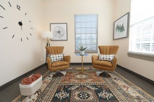 TMS therapy waiting area with two tan armchairs, round side table, geometric wall clock, and patterned rug