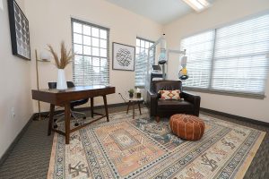 TMS therapy office space with wooden desk, black sofa, hanging exercise equipment, and orange pouf ottoman