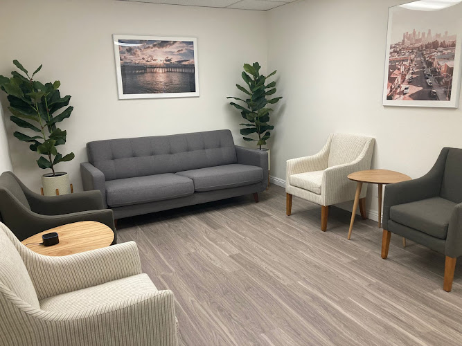 Modern waiting room with gray sofa, cream chairs, potted plants, and framed coastal artwork